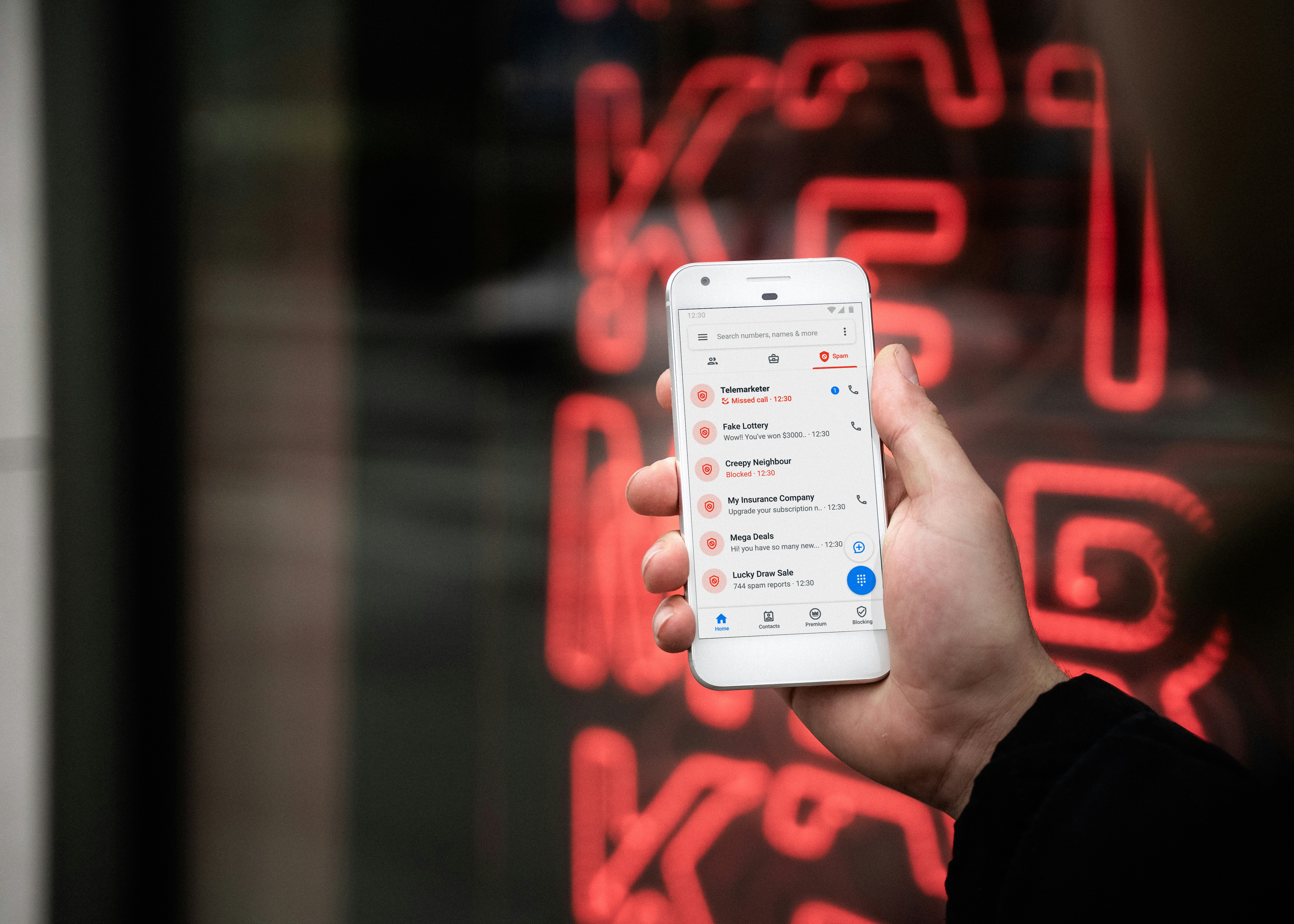 Person holding a smartphone displaying a list of spam calls and messages with a neon background.